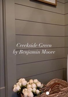 there is a basket with white flowers on the floor next to a wall that reads, crocksdale green by bennum moore