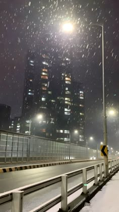 a city street at night with snow falling on the ground and buildings in the background