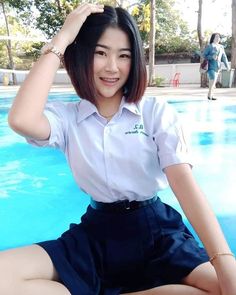 a woman sitting on the ground next to a swimming pool wearing a white shirt and blue skirt