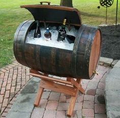 a wooden barrel with bottles in it sitting on top of a brick walkway next to a tree