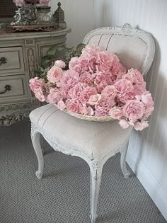 pink flowers are in a basket on an old chair