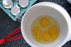 three eggs are in a white bowl with red whisks next to them on a table