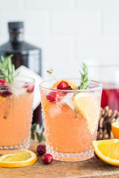 two glasses filled with oranges and cranberries on top of a wooden table