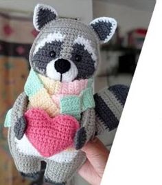 a crocheted stuffed raccoon holding a heart