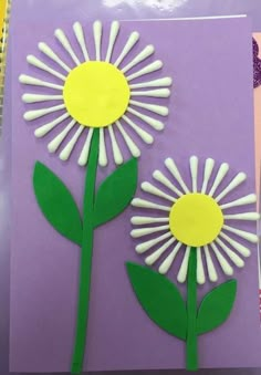 two paper flowers with green stems on purple background, one is cut out and the other is made from construction paper