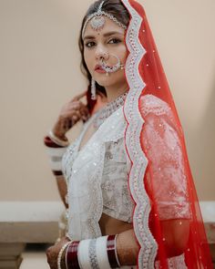 a woman wearing a red and white bridal outfit with veil on her head is posing for the camera