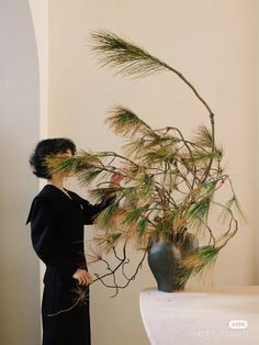 a woman standing in front of a vase with some plants on it's side