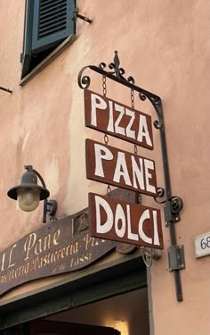 a restaurant sign hanging from the side of a pink building with green shutters on it's windows