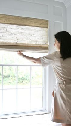 a woman standing in front of a window looking out the window with her hand on the blinds