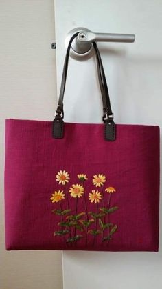 a pink bag with yellow daisies on it hanging from a hook in front of a white wall