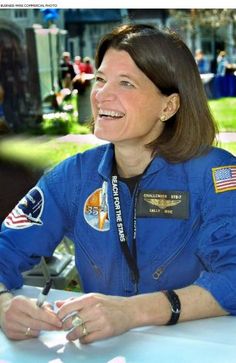 a woman in an astronaut's uniform smiles while sitting at a table with other people