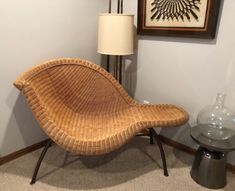 a wicker lounge chair next to a lamp in a room with pictures on the wall