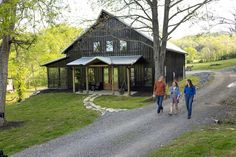 three people walking down a dirt road towards a house