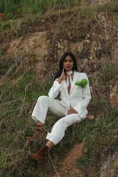 a woman sitting in the grass with her hand on her face and holding a green plant