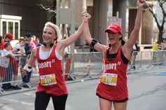 two women in red shirts and black pants are running with their arms up as people watch from the sidelines