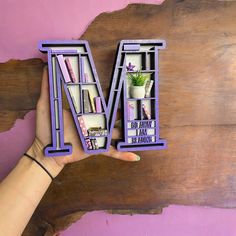 a person holding up some type of letter m with bookshelves on it's sides