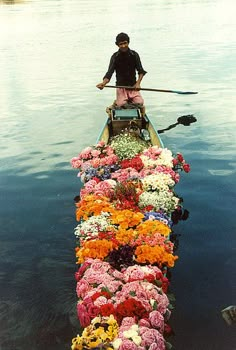 a man rowing a boat filled with lots of flowers