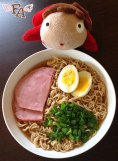 a bowl of ramen with an egg, ham and green onions in it next to a stuffed animal