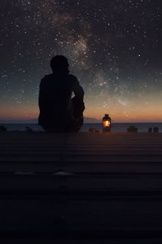 a person sitting on a dock looking at the night sky with stars in the background