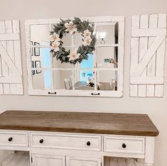 a white dresser with two mirrors on top of it and a wreath hanging from the wall