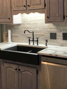 a kitchen with wooden cabinets and marble counter tops, black double - basin sink, and stainless steel dishwasher