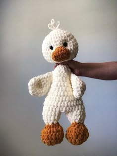 a crocheted stuffed duck is being held by a person's hand in front of a gray background