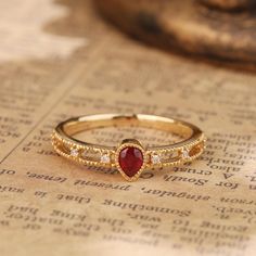 a red stone ring sitting on top of a piece of paper next to a book