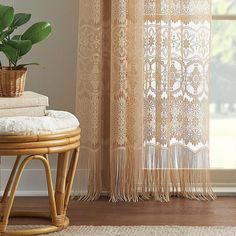 a plant in a basket on top of a stool next to a window with sheer curtains