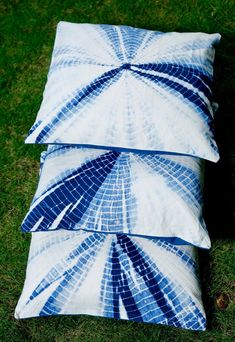 three pillows sitting on top of each other in the grass with blue and white designs