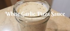 a white garlic pizza sauce in a glass jar on a counter top with the words white garlic pizza sauce above it