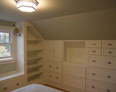 an empty bedroom with white cabinets and drawers in the corner, next to a window