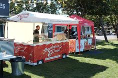 a food truck is parked on the grass near some trees and people are standing outside