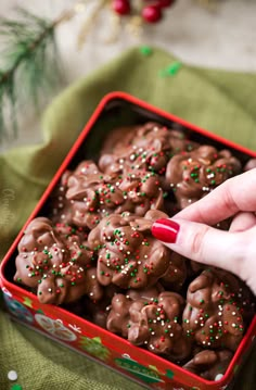 a woman's hand reaching for chocolate covered cookies in a red box with sprinkles