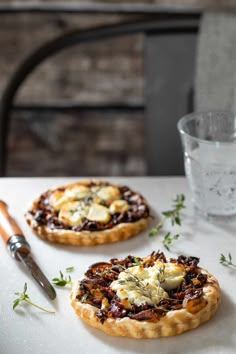 two pies sitting on top of a white table next to a glass of water