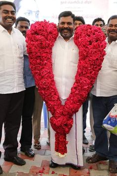 a group of men standing next to each other near a heart shaped flower arrangement on the ground