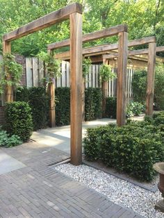 a wooden pergolated area surrounded by plants and rocks in the middle of a brick walkway