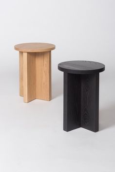 two wooden stools sitting next to each other on a white surface, one black and one light brown