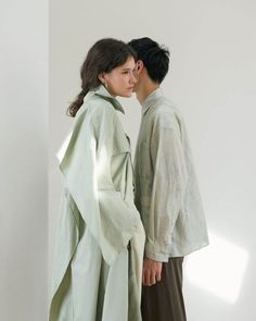 two people standing next to each other in front of a white wall and one is wearing a green coat