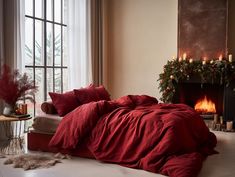 a bed with red sheets and pillows next to a fire place in a living room