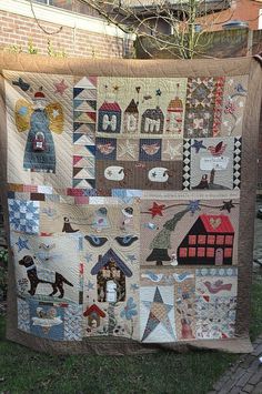 a quilt hanging on the side of a brick building in front of a tree and fence