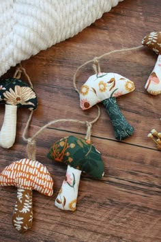 small mushrooms are hanging from twine strings on a wooden floor with white blanket and pillow in the background