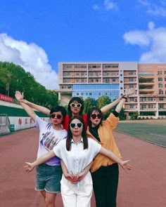 four people standing on a tennis court with their arms in the air while wearing sunglasses