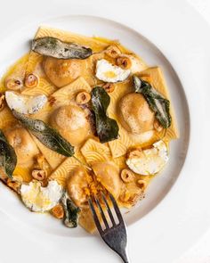 a white plate topped with pasta covered in cheese and spinach leaves next to a fork