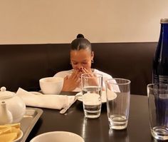 a woman sitting at a table covered in food and drinking from a cup with her hands