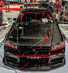 a black car with red stripes parked in front of other cars on display at an auto show