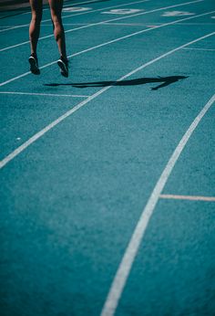 a person running across a blue track with white lines on the ground and one foot in the air