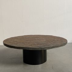 a round wooden table sitting on top of a cement floor next to a white wall