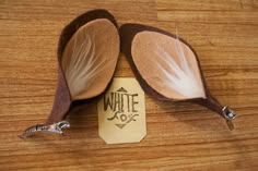 two brown and white feathered spoons sitting on top of a wooden table next to a tag