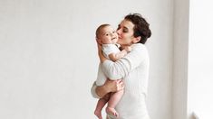 a woman holding a baby in her arms and kissing it's face with both hands