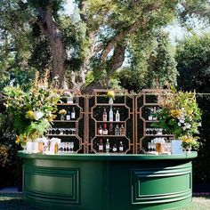 an outdoor bar with flowers and bottles on the top, in front of a tree